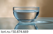 Clear glass bowl filled with water reflecting soft natural light. Стоковое AI-изображение, AI-художник Katsiaryna Repich / Фотобанк Лори