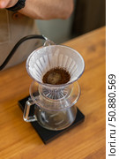 A person brews coffee using a pour-over method. The setup includes a glass dripper, coffee grounds, and a scale on a wooden table. Стоковое фото, фотограф PAv / Фотобанк Лори