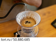 A close-up of coffee brewing in a pour-over dripper. The coffee grounds are dark and wet, with a rich brown liquid dripping into a clear carafe below. Стоковое фото, фотограф PAv / Фотобанк Лори