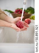 Close up view of a woman washes red peach under the pressure of flowing water in the white kitchen, a basket with radishes, broccoli and onions in the background, washed green grapes in a cup. Стоковое фото, фотограф Vladimir Drozdin / Фотобанк Лори