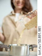 A girl pours white rice from a glass jar into a metal pot. Стоковое фото, фотограф Vladimir Drozdin / Фотобанк Лори