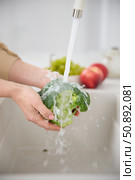 Close up view of a woman washes broccoli under the pressure of flowing water in the white kitchen, tomatoes and green grapes in the background. Стоковое фото, фотограф Vladimir Drozdin / Фотобанк Лори