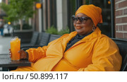 A joyful woman in bright orange attire enjoys a refreshing drink at an outdoor urban cafe during a sunny day. Стоковое AI-видео, аниматор Данила Большаков / Фотобанк Лори