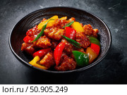Sweet sour pork with colorful peppers, mixed vegetables served in a black bowl on dark concrete background. Traditional Chinese dish. Close-up. The meat pieces in a brown sauce glaze. Sichuan cuisine. Стоковое AI-изображение, AI-художник Марина Демидюк / Фотобанк Лори