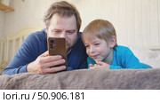 Father and son little boy laughing and using phone. They watching funny videos together, playing games on smartphone. Concept technology, smartphone addicted. Fun weekend activity. Modern fatherhood. Стоковое видео, видеограф Марина Демидюк / Фотобанк Лори