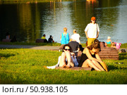 Young girls sunbathing on a green lawn on the shore of a pond in Kuzminki Park. Russia. Moscow. 25.07.25. Редакционное фото, фотограф Ярославский Максим / Фотобанк Лори