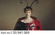 Fashion model wearing ladybug inspired costume with antennae and red and black polka dot cape posing in a studio setting with a textured background. Стоковое AI-видео, аниматор Данил Руденко / Фотобанк Лори