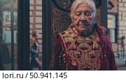 Senior woman in elaborate traditional dress posing gracefully near ornate wooden doorway, radiating vintage sophistication and cultural heritage. Стоковое AI-видео, аниматор Данил Руденко / Фотобанк Лори