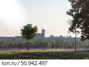 A lone man stands in a peaceful, grassy park at sunrise, gazing at the distant Belgrade skyline. Стоковое фото, фотограф Виктор Ветошкин / Фотобанк Лори