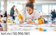 A young female artist intently working on a colorful artwork in a bright art studio setting, expressing creativity. Стоковое AI-изображение, AI-художник Данила Большаков / Фотобанк Лори