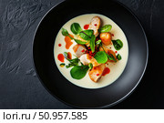 An artful overhead shot of Tom Kha Kai in a black bowl highlights the contrast between its milky broth and vibrant toppings. This presentation showcases traditional Thai culinary artistry. Стоковое AI-изображение, AI-художник Nart / Фотобанк Лори
