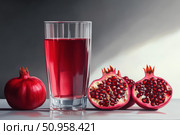Freshly squeezed pomegranate juice in a clear glass, surrounded by ripe split pomegranates and scattered seeds on a white surface. Rich red tones, natural light, clean composition. Copy space. Стоковое AI-изображение, AI-художник Евгений Демидюк / Фотобанк Лори