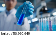 Scientist conducts experiment with blue liquid in laboratory surrounded by test tubes and scientific equipment. Стоковое AI-изображение, AI-художник Сергей Толмачёв / Фотобанк Лори