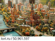 A detailed model of a cityscape with elements of classical Russian architecture. In the foreground are miniature copies of churches, towers and residential buildings in bright autumn colours. A bridge over the river, cobbled streets and various vegetation are visible. The composition conveys the atmosphere of the historical centre of a large city. Suitable for themes of urban studies, architecture, modelling and cultural heritage. Стоковое AI-изображение, AI-художник Анна Кривицкая / Фотобанк Лори