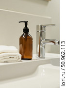 In a tranquil bathroom setting, a sleek sink stands beside a glass bottle of liquid soap and a neatly folded towel, showcasing a blend of simplicity and elegance Generative AI. Стоковое AI-изображение, AI-художник Юлия Петровская / Фотобанк Лори