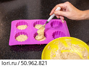 A hand carefully spoons batter into a silicone baking pan, preparing individual servings of banana muffins. Стоковое фото, фотограф Коханова Наталья / Фотобанк Лори