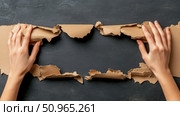 Human hands tearing open craft paper to unveil a dark textured wall, creating a dynamic frame for a message or product announcement, concept of revelation and fresh opportunity. Стоковое AI-изображение, AI-художник Данила Большаков / Фотобанк Лори