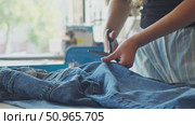 With the help of scissors, a woman is cutting denim fabric in order to modernize her clothes at home. Стоковое видео, видеограф Strunov David / Фотобанк Лори