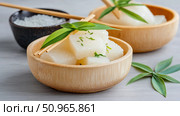 Elegant presentation of refreshing white translucent food cubes garnished with green herbs in a natural wooden bowl, embodying healthy Asian cuisine. Стоковое AI-изображение, AI-художник Данила Большаков / Фотобанк Лори