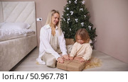 Mom and little toddler daughter sit on a floor in bedroom, open New Year gift box near the Christmas tree. Merry Christmas and Happy New Year winter holidays. Festive home interior. Стоковое видео, видеограф Ирина Михайличенко / Фотобанк Лори