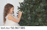 Happy beautiful little girl in elegant white fluffy dress stands near a Christmas tree at home, laughing joyfully in anticipation of winter holiday. New year, fairy tales and children dreams footage. Стоковое видео, видеограф Ирина Михайличенко / Фотобанк Лори