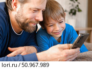 Father and son little boy laughing and using phone. They watching funny videos together, playing games on smartphone. Concept technology, smart phone addicted. Fun weekend activity. Modern fatherhood. Стоковое фото, фотограф Марина Демидюк / Фотобанк Лори