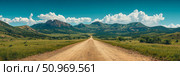 Panoramic view of a rustic dirt road disappearing into the horizon amidst lush green valleys and towering mountains under a beautiful clear blue sky with puffy white clouds. Стоковое AI-изображение, AI-художник Данила Большаков / Фотобанк Лори