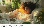 Serene young woman in bed using a laptop, bathed in warm sunlight with surrounding greenery and plants, creating a peaceful and cozy ambiance. Стоковое AI-видео, аниматор Данила Большаков / Фотобанк Лори