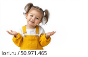 Child in yellow overalls smiles and gestures with hands indoors. Стоковое AI-изображение, AI-художник Katsiaryna Repich / Фотобанк Лори