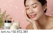 Woman with a relaxed expression enjoys skincare routine, surrounded by jars of cream, on a soft pink background. Highlighting self-care and beauty products. Стоковое AI-изображение, AI-художник lyudmila Soloveva / Фотобанк Лори