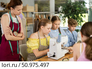 Schoolgirl practicing stitching at machine under guidance of instructor at lesson. Стоковое фото, фотограф Яков Филимонов / Фотобанк Лори