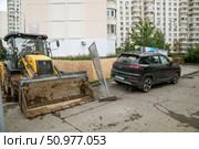 Во дворе жилого дома экскаватор с опущенным ковшом стоит рядом с легковым автомобилем. Между ними строители оставили одинокую покосившуюся секцию сигнального ограждения. Москва, улица Большая Марфинская, дом 1 корпус 2. Редакционное фото, фотограф Наталья Николаева / Фотобанк Лори