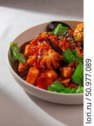 Traditional Korean tteokbokki with seafood mix including mussels, baby octopus, spicy sauce, boiled egg and sesame served in a ceramic bowl under natural daylight. Стоковое фото, фотограф Aleksandr Gavrilychev / Фотобанк Лори
