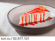 Soft cheesecake with graham crust and strawberry syrup topped with an edible flower on ceramic plate under soft natural light. Стоковое фото, фотограф Aleksandr Gavrilychev / Фотобанк Лори