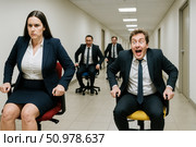 Happy employees having fun riding on chairs in office hallway. Business people competing in funny race during corporate event. Стоковое AI-изображение, AI-художник Павел Муравьев / Фотобанк Лори