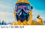 Intense close-up of person wearing bright yellow hazmat suit and full-face gas mask, highlighting safety and preparedness for hazardous conditions or biohazard protection in outdoor setting. Стоковое AI-изображение, AI-художник Данила Большаков / Фотобанк Лори
