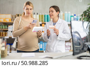 Expecting woman comparing supplements using phone at drugstore. Стоковое фото, фотограф Яков Филимонов / Фотобанк Лори