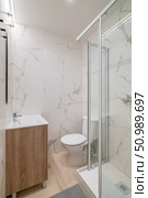 Modern bathroom with a glass shower, white toilet, and wooden vanity. Marble-patterned walls create a sleek, contemporary look. Стоковое фото, фотограф PAv / Фотобанк Лори