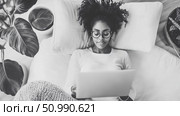 Black woman relaxing on a comfy bed using a laptop, monochrome aesthetic. Стоковое AI-изображение, AI-художник Данила Большаков / Фотобанк Лори