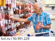 mature senor choosing uncooked smoked sausages in sausage department supermarket. Стоковое фото, фотограф Татьяна Яцевич / Фотобанк Лори
