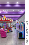 Carousel and arcade games shining under purple ceiling lights in entertainment center. Стоковое фото, фотограф Юрий Поздников / Фотобанк Лори
