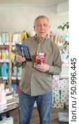 Elderly man is standing in a supermarket and holding razors from different manufacturers in hands, he is reading the instructions and manufacturing materials. Mature man chooses a trimmer and an electric shaver. Стоковое видео, видеограф Яков Филимонов / Фотобанк Лори