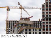 Building development process: Cranes amidst buildings under construction against an overcast sky. Стоковое фото, фотограф Данила Большаков / Фотобанк Лори