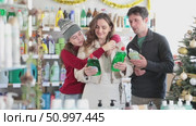 Friendly family of three shopping for dishwashing detergent in decorated store during Christmas season, carefully comparing different products. Стоковое видео, видеограф Яков Филимонов / Фотобанк Лори