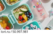 Overhead view of light blue lunch containers holding quinoa, cucumber, blueberries, tomatoes, bell peppers beside pink water bottle, representing nutritious midday eating. Стоковое AI-видео, аниматор Данил Руденко / Фотобанк Лори