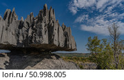 A karst rock with bizarre outlines. Steep furrowed slopes, sharp spiny peaks. Close-up. Green vegetation in the valley in the distance. Blue sky, clouds. Madagascar. Tsingy De Bemaraha (2023 год). Стоковое фото, фотограф Вера Ивановна Кубарева / Фотобанк Лори