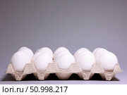 Большой картонный лоток, полный свежих белых куриных яиц, на сером фоне. Концепция запаса продуктов и покупки в магазине. Стоковое фото, фотограф Евгений Ковальский / Фотобанк Лори