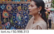 Seasoned Indian astrologer pointing at detailed natal chart wheel, explaining zodiac signs amid curious crowd during spiritual esoteric event. Стоковое AI-видео, аниматор Данил Руденко / Фотобанк Лори