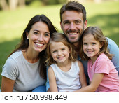 A joyful family gathers in a sunny park, with the parents happily embracing their two daughters. They share laughter, smiles, and a moment of togetherness in natures beauty Generative AI. Стоковое AI-изображение, AI-художник Юлия Петровская / Фотобанк Лори