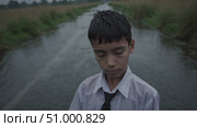 Soaked student wearing white shirt and tie standing near river during monsoon, expressing deep melancholy and introspective mood of youthful struggle. Стоковое AI-видео, аниматор Данил Руденко / Фотобанк Лори